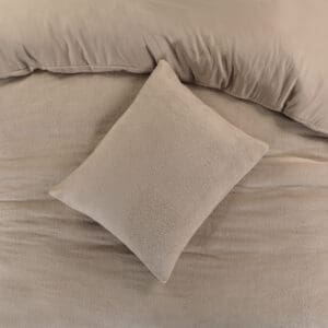Beige kussen op bed met dekbed.