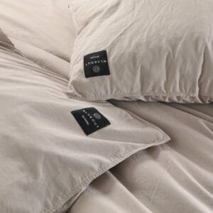 Beige beddengoed met zwarte labels op een bed.